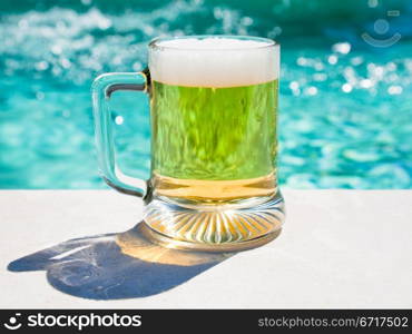 glass of cold beer on pool board in hot summer day