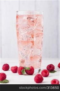 Glass of cold raspberry cider with ice cubes and fresh berries on light wooden background
