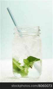 glass of cold water with fresh mint leaves and ice cubes on turquoise background