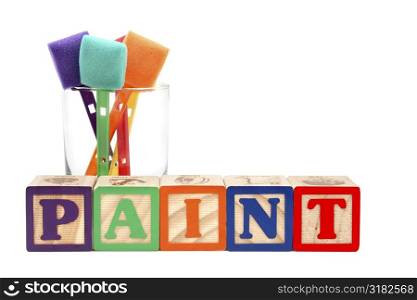 Glass of colorful paint sponges behind the word &acute;paint&acute; spelt with alphabet blocks.