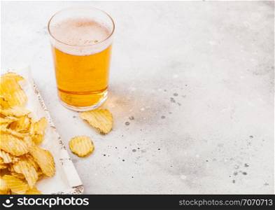 Glass of craft lager beer with potato crisps snack in vintage wooden box and opener on stone kitchen background. Beer and snack