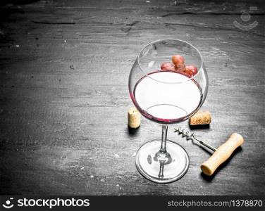 glass of cran wine with a corkscrew and a branch of grapes. On the black chalkboard.. glass of cran wine with a corkscrew and a branch of grapes.