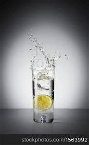 Glass of crystal clear water and a slice of lime falling in making big splash. Lime in a glass