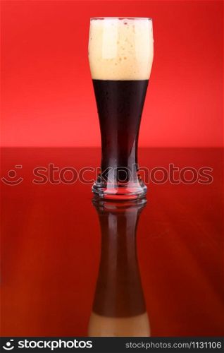 Glass of dark beer over a bright red background