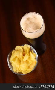 Glass of dark beer with snacks on a wooden table