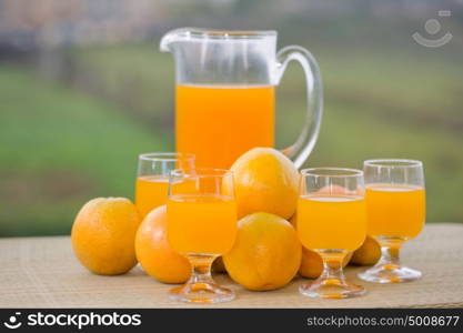 glass of delicious orange juice and oranges on table in garden