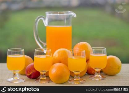 glass of delicious orange juice and oranges on table in garden