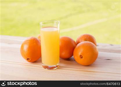 glass of delicious orange juice and oranges on table in garden. orange juice