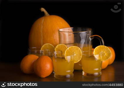 glass of delicious orange juice with oranges and a pumpkin on a table, studio picture