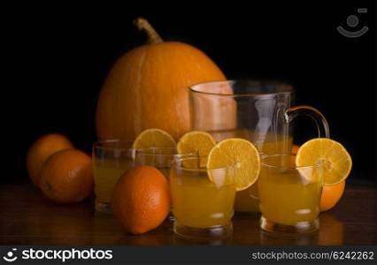 glass of delicious orange juice with oranges and a pumpkin on a table, studio picture