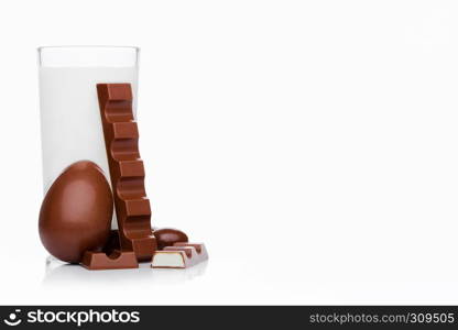 Glass of fresh breakfast milk with chocolate bar egg and candies on white background