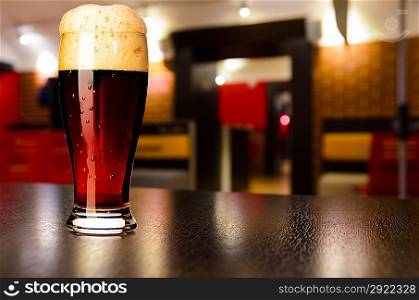glass of fresh draft dark beer on table in pub
