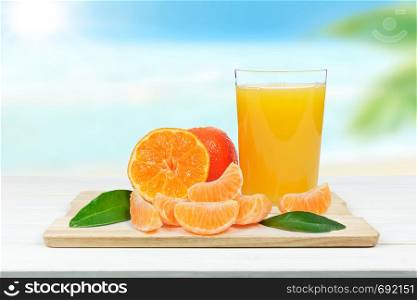 Glass of fresh orange juice and orange or tangerine fruits with leaves on blurred background of a tropical beach (mixed)