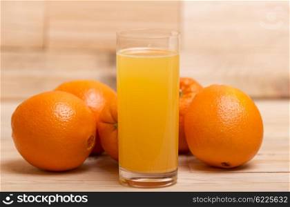 glass of fresh orange juice and oranges on a wooden background