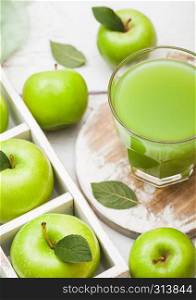 Glass of fresh organic apple juice with granny smith green apples in box on wood background.