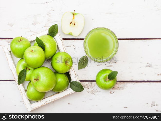 Glass of fresh organic apple juice with green apples in box on wood background.