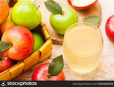 Glass of fresh organic apple juice with red and green apples in vintage basket on wood background