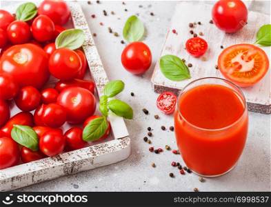 Glass of fresh organic tomato juice with fresh raw tomatoes basil and pepper in box on stone background