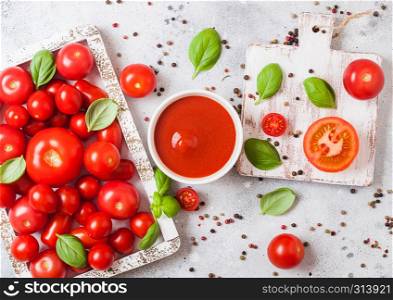 Glass of fresh organic tomato paste with fresh raw tomatoes basil and pepper in box on stone background