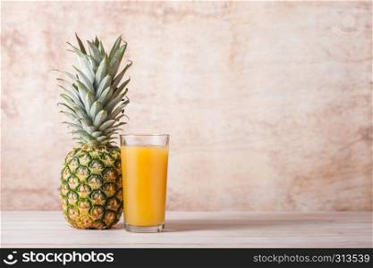 Glass of fresh pineapple juice with raw fruit on wooden background
