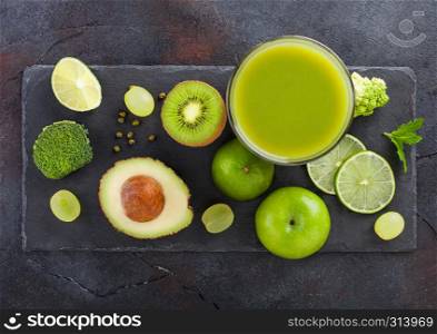 Glass of fresh raw organic green toned fruit and vegetables on stone board background. Avocado, lime, apple, kiwi and grapes with broccoli and cauliflower