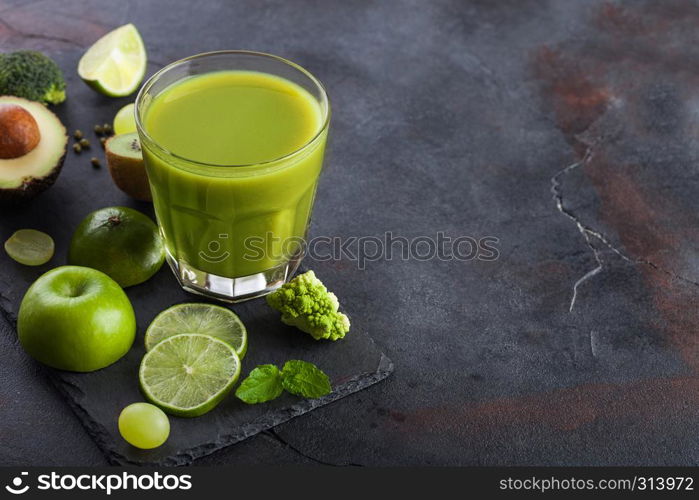 Glass of fresh raw organic green toned fruit and vegetables on stone board background. Avocado, lime, apple, kiwi and grapes with broccoli and cauliflower