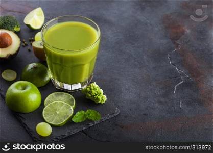 Glass of fresh raw organic green toned fruit and vegetables on stone board background. Avocado, lime, apple, kiwi and grapes with broccoli and cauliflower