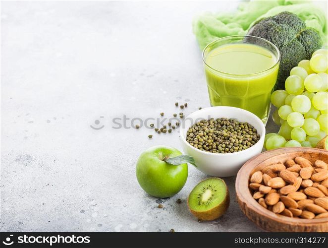 Glass of fresh smoothie juice organic green toned fruit and vegetables on stone kitchen table background. With almond nuts in bowl.