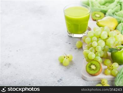 Glass of fresh smoothie organic green toned fruit on white chopping board on stone background. Pear and grapes with kiwi and lime and apple.