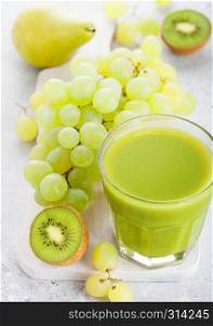 Glass of fresh smoothie organic green toned fruit on white chopping board on stone background. Pear and grapes with kiwi and lime and apple.