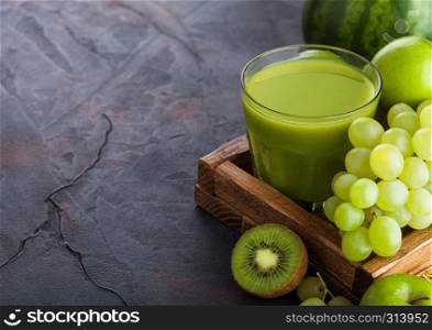 Glass of fresh smoothie with organic green toned fruits in white vintage box on stone kitchen table background. Pear and grapes with kiwi and lime with apple.