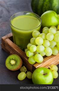 Glass of fresh smoothie with organic green toned fruits in white vintage box on stone kitchen table background. Pear and grapes with kiwi and lime with apple.
