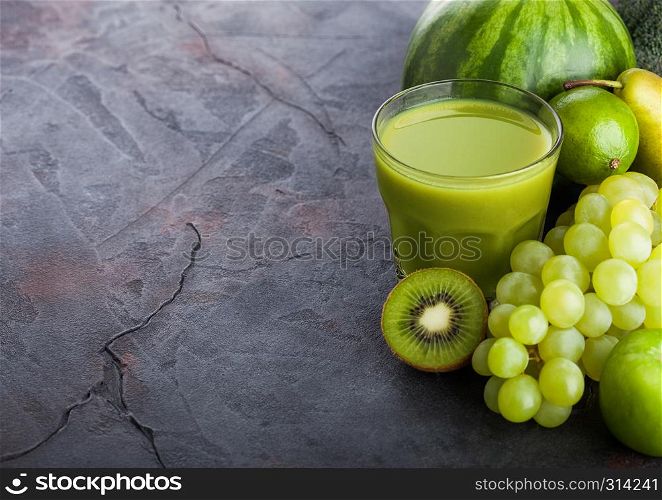 Glass of fresh smoothie with organic green toned fruits on stone kitchen table background. Pear and grapes with kiwi and lime with apple.