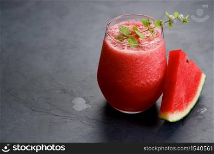 Glass of healthy watermelon smoothie with mint leaves on dark background