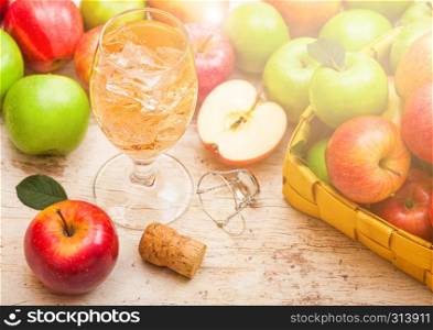 Glass of homemade organic apple cider with fresh apples in bamboo basket on wooden background, Glass with ice cubes