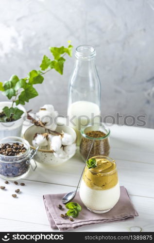 Glass of Iced Dalgona Coffee, a trendy fluffy creamy whipped coffee, decorated by mint and ingredients on light rustic background, copy space.