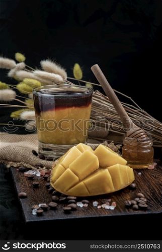 Glass of Iced tropical Mango smoothie mixed Espresso coffee served with Honey on the Wooden cutting board and Dark background. Alternative summer drink for living life, Selective focus.