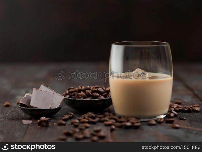 Glass of Irish cream baileys liqueur with coffee beans and dark chocolate in steel bowl on dark wood background. Space for text