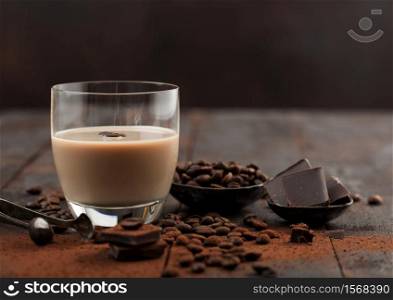 Glass of Irish cream baileys liqueur with coffee beans and powder with dark chocolate on dark wood background. Space for text