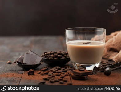 Glass of Irish cream baileys liqueur with coffee beans and powder with dark chocolate on dark wood background. Space for text