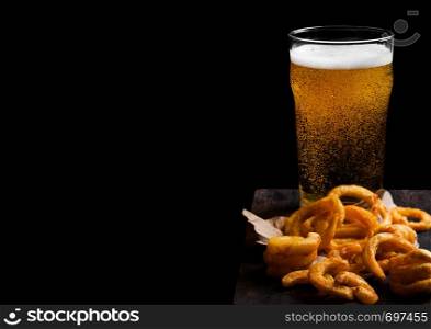 Glass of lager beer with curly fries snack on vintage wooden board on black.