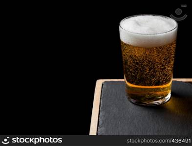 Glass of lager beer with foam and bubbles on stone board on black. Space for text