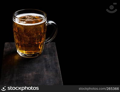 Glass of lager beer with foam and bubbles on vintage wooden board on black. Space for text