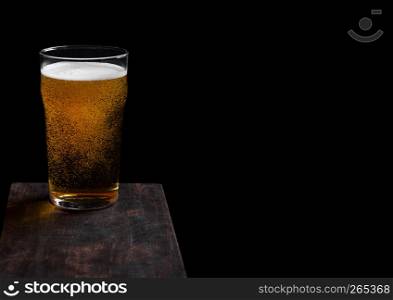 Glass of lager beer with foam and bubbles on vintage wooden board on black. Space for text