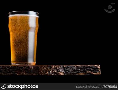 Glass of lager beer with foam and bubbles on vintage wooden board on black.