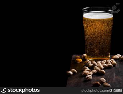 Glass of lager beer with pistachios nuts on stone board on black background.