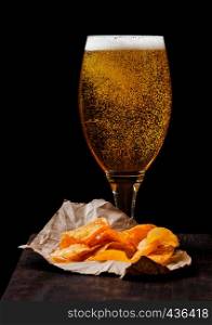 Glass of lager beer with potato crisps snack on vintage wooden board on black background.