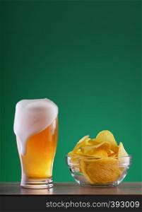 Glass of light beer with drip foam and a plate of chips on a green background. Glass of light beer with drip foam and plate of chips