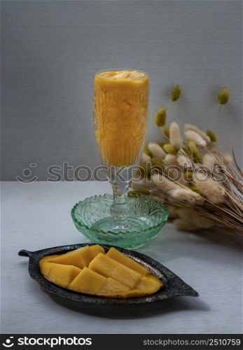 Glass of Mango shake with Fresh ripe yellow mango fruit. Fresh tropical fruit smoothies on white background. Healthy detox herbal drink, Fruit on the summer season, Space for text, Selective focus.