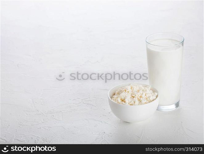 Glass of milk and bowl of cottage cheese on white stone kitchen table background.